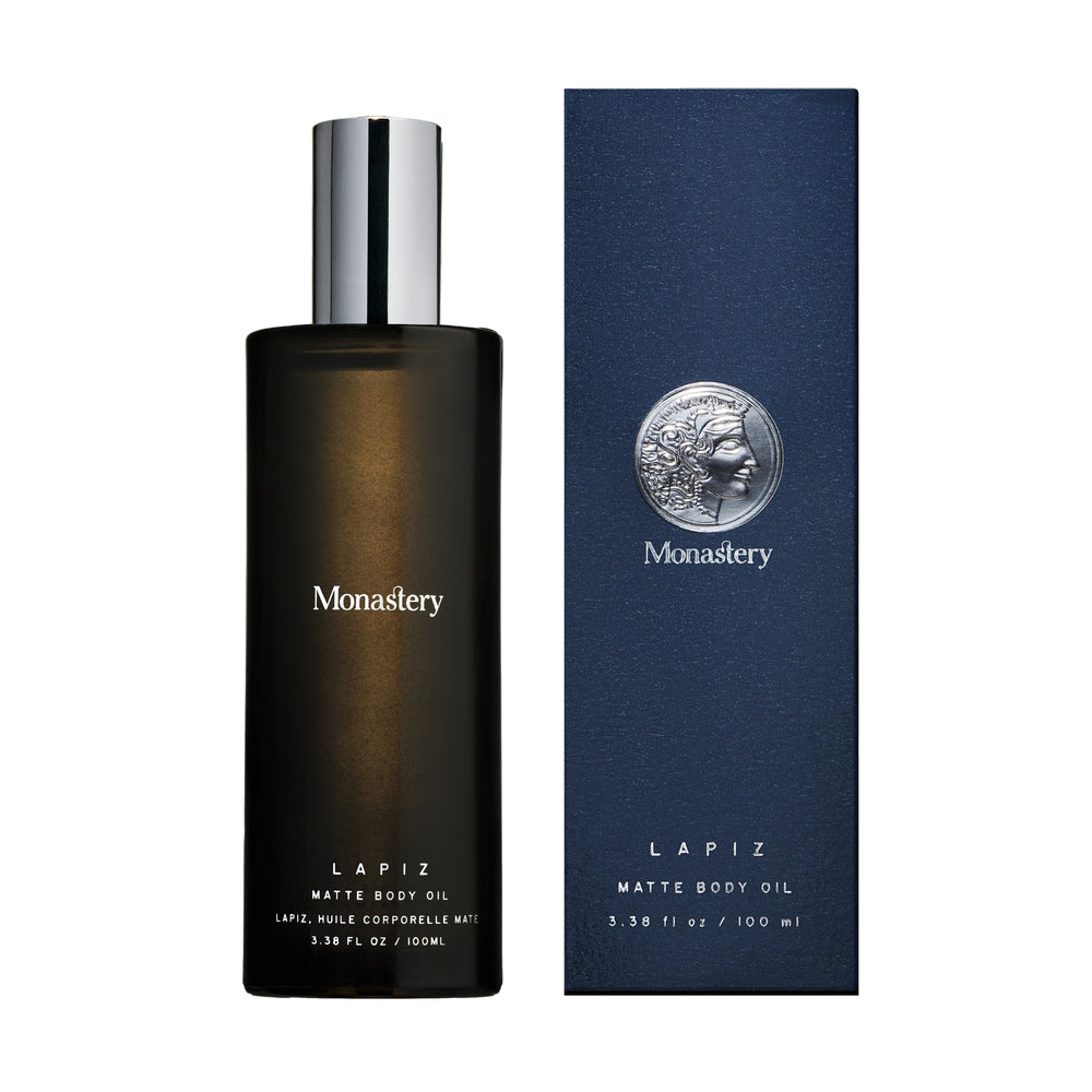 Lapiz matte body oil from Monastery in glass bottle with silver cap and box next to it on white background