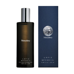 Lapiz matte body oil from Monastery in glass bottle with silver cap and box next to it on white background