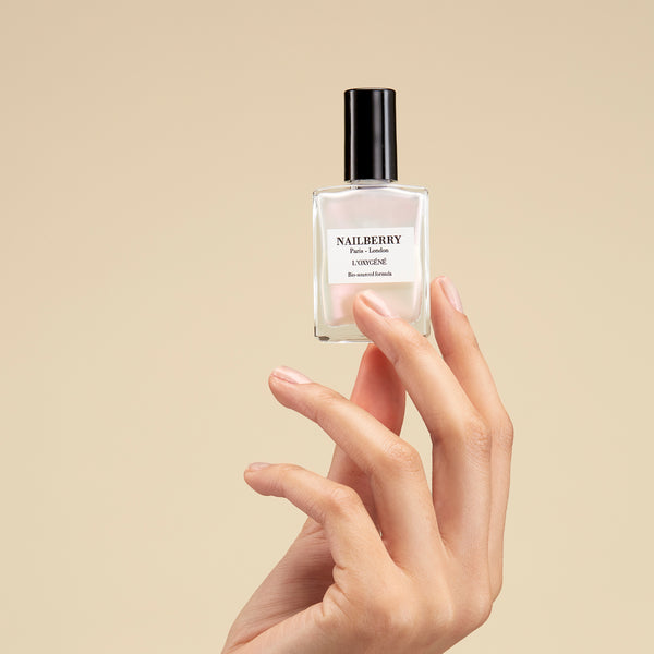 Hand holding a Nailberry nail polish bottle against a beige background