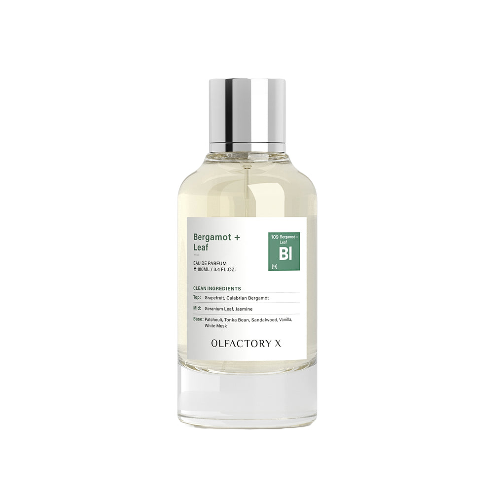 A bottle of Olfactory X Bergamot + Leaf 100% natural perfume with a clear glass body, light yellow liquid, a white label with green accents, and a reflective silver cap, set against a plain white background.