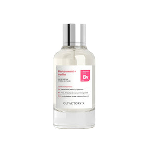 A clear glass bottle of Olfactory X Blackcurrant + Vanilla Eau de Parfum with a reflective silver cap and a white label featuring pink accents, set against a plain white background.