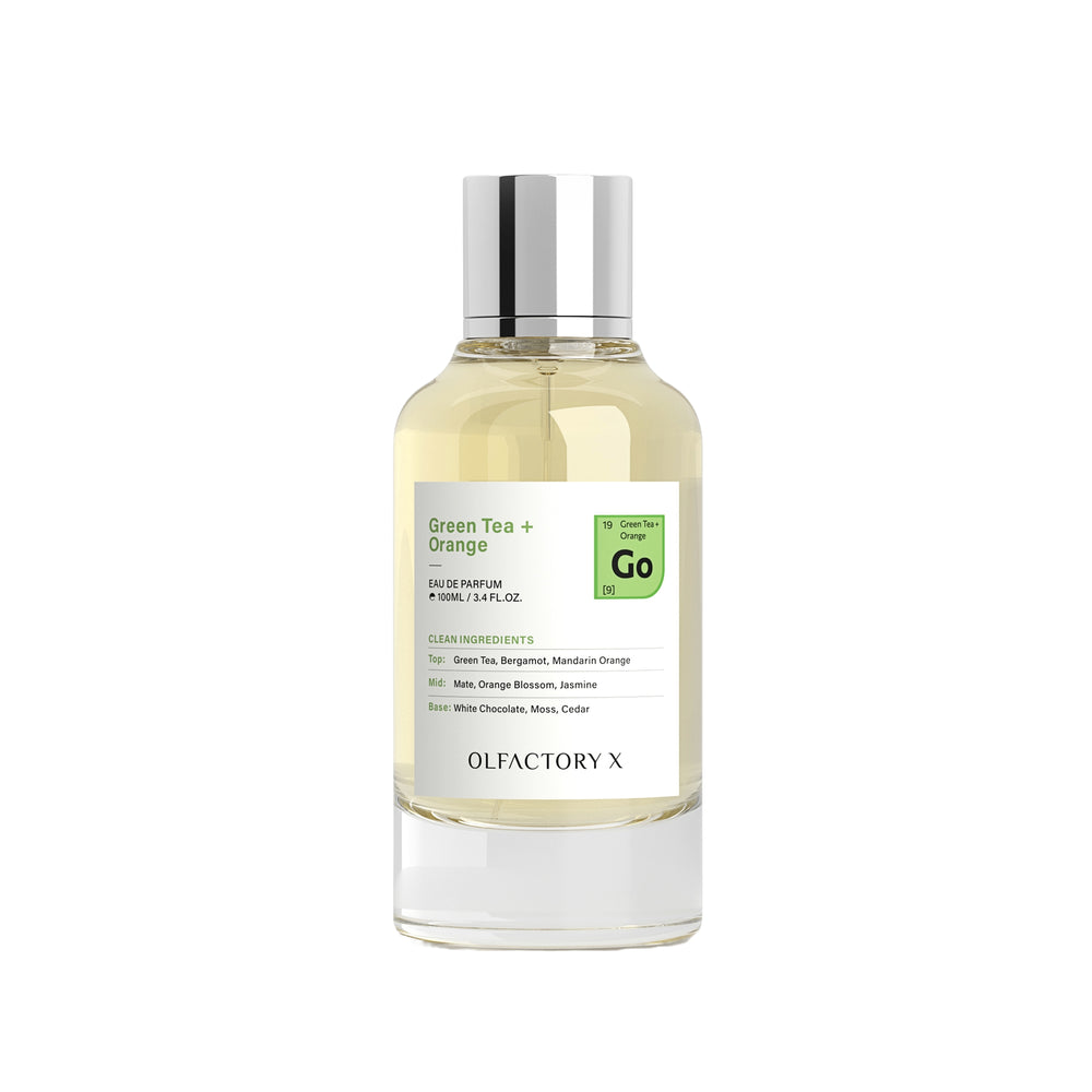 A clear glass bottle of Olfactory X Green Tea + Orange Eau de Parfum with a silver cap, containing a pale yellow liquid, set against a plain white background.