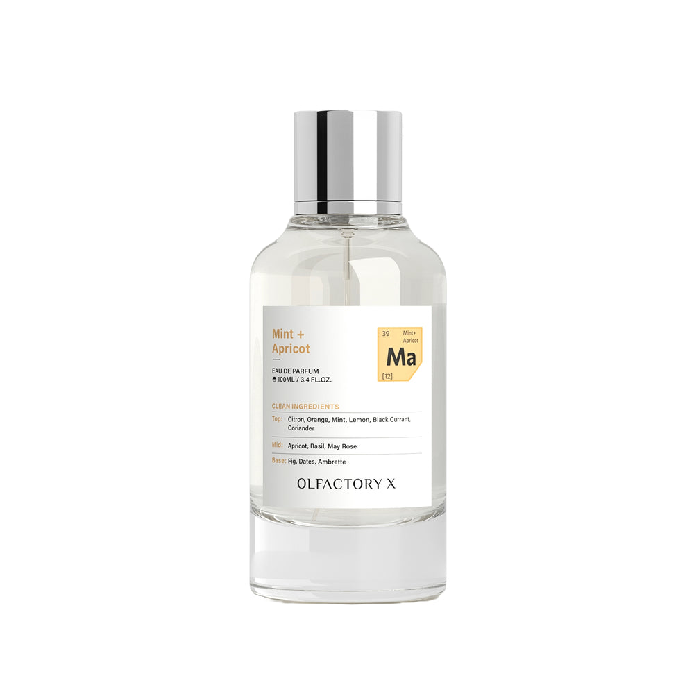 A clear glass bottle of Olfactory X Mint + Apricot Eau de Parfum with a reflective silver cap and a white label featuring a gold periodic table accent.