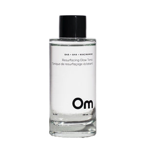 Clear bottle of Om skincare tonic with black cap on a white background