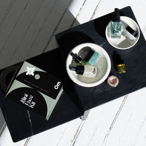 Cosmetic products on a black tray with 'Om Organics' branding on a black surface