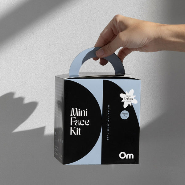 Hand holding a 'Mini Face Kit' box with 'Om' branding on a gray background