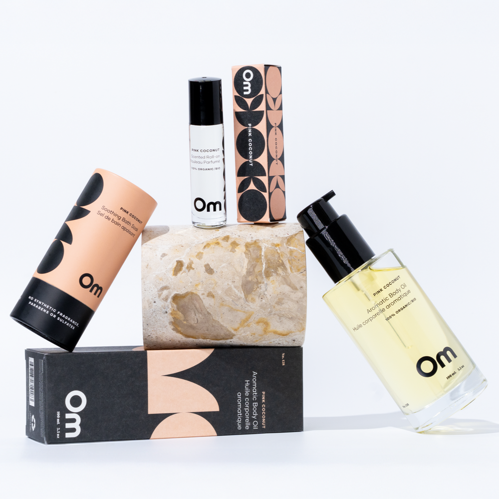 OM Organics Pink Coconut body care set with aromatic body oil, scented roll-on, and soothing bath soak displayed together.