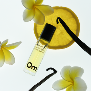 OM ORGANICS Sunset Nectar Scented Roll On surrounded by plumeria flowers, vanilla bean stocks and lemon slice