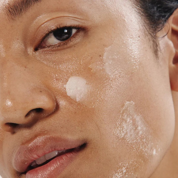 Close-up of a person's face with a skincare product applied to the cheek. the product is OM ORGANICS Tahiti Lime + Babassu Radiant Cleansing Balm