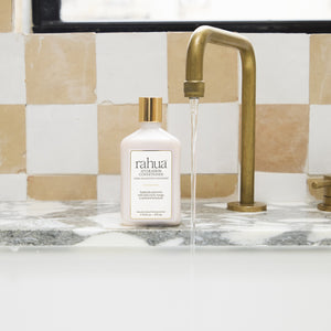 Rahua hydration conditioner on a bathroom counter with a running faucet against a checkered backsplash.