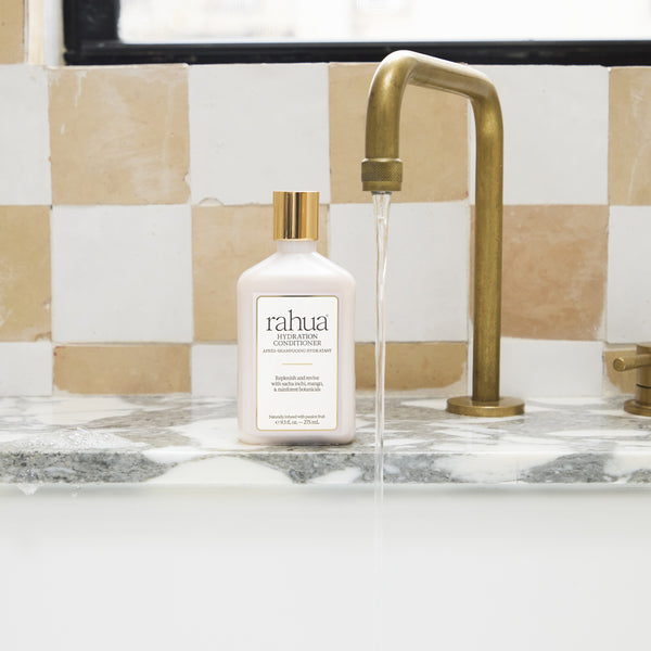 Rahua hydration conditioner on a bathroom counter with a running faucet against a checkered backsplash.