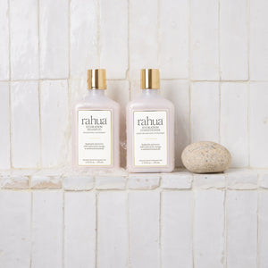 Two bottles of rahua shampoo and conditioner on a tiled bathroom wall.
