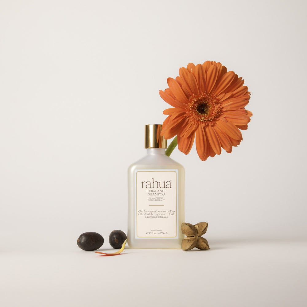 A bottle of Rahua Rebalance Shampoo with a white body, a metallic gold cap, and a cream-colored label with a light blue border, set against a plain white background.