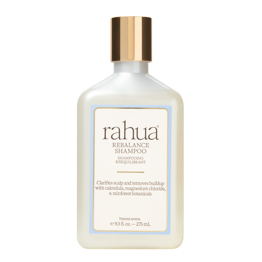 A bottle of Rahua Rebalance Shampoo with a white body, a metallic gold cap, and a cream-colored label with a light blue border, set against a plain white background.
