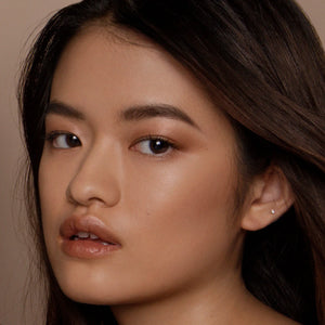 Close-up of a person with dark hair and neutral makeup against a beige background. RITUEL DE FILLE Inner Glow Crème Pigment Eros