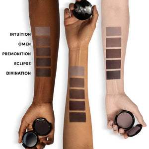 Three arms with swatches of makeup products labeled 'Intuition', 'Omen', 'Premonition', 'Eclipse', and 'Divination'.
