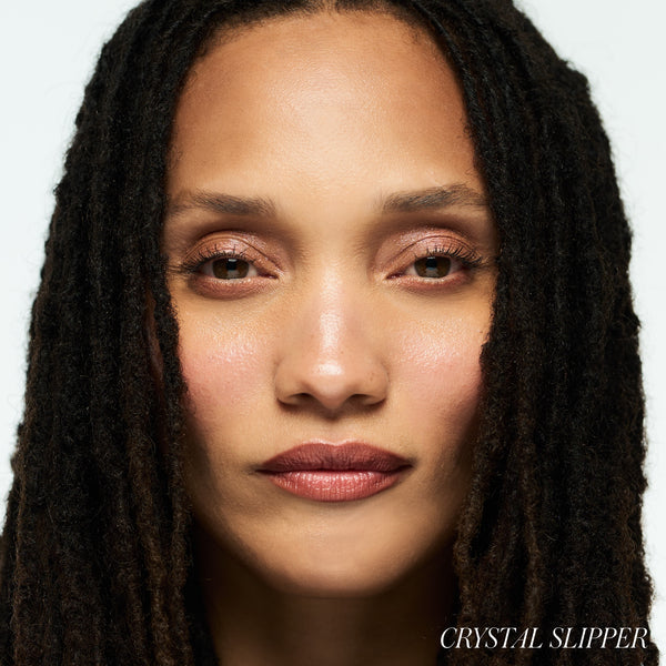 Close-up of a woman with dark hair against a white background wearing RMS BEAUTY Luminizer Crystal Slipper