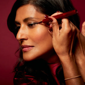 Woman applying eyeliner with a red eyeliner brush against a red background
