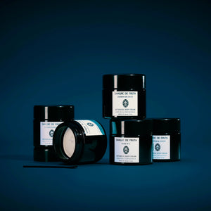 Set of black jars of Sangre de Fruts body creams with white labels on a dark blue background