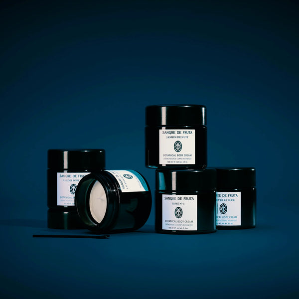 Set of black jars of Sangre de Fruts body creams with white labels on a dark blue background