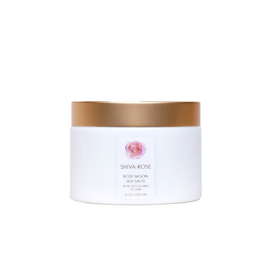 Shiva Rose Rose Moon Sea Salts in a decorative container, surrounded by dried rose buds and essential oils, emphasizing a luxurious bathing experience.
