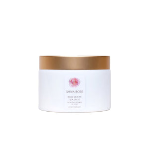 Shiva Rose Rose Moon Sea Salts in a decorative container, surrounded by dried rose buds and essential oils, emphasizing a luxurious bathing experience.