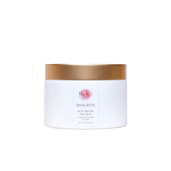 Shiva Rose Rose Moon Sea Salts in a decorative container, surrounded by dried rose buds and essential oils, emphasizing a luxurious bathing experience.