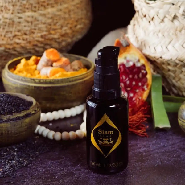 Black bottle with pump with gold logo labeled 'SIAM SEAS Twilight BeCalm Skin Serum' on a dark surface with natural elements in the background.