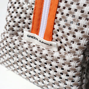 Close-up of a woven bag with orange and white straps and 'Green Jungle' label.