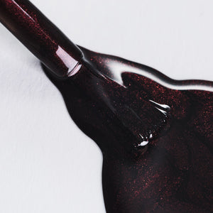 Close-up of dark red glittery nail polish on a white background