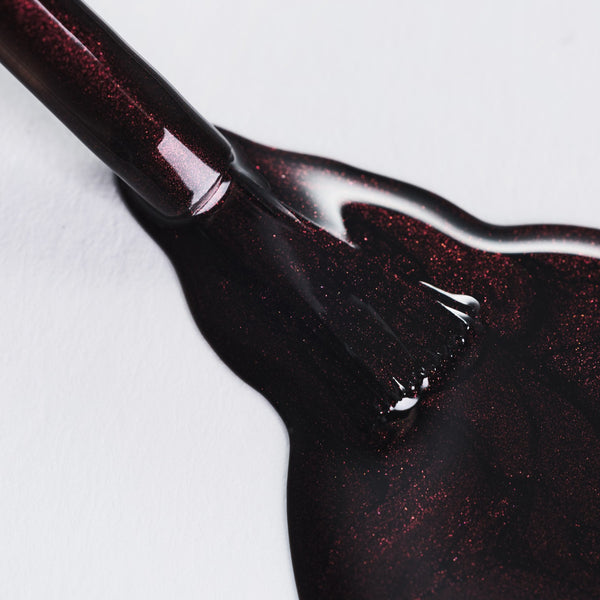 Close-up of dark red glittery nail polish on a white background