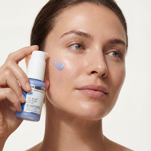 Woman applying skincare product to her face with a neutral background