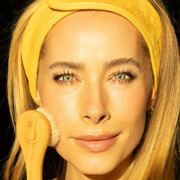 Woman with a yellow headband holding a makeup brush against a black background