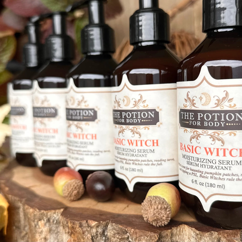THE POTION COSMETICS Basic Witch Body Potion bottle surrounded by autumn leaves, highlighting pumpkin, coffee, vanilla, and patchouli notes.