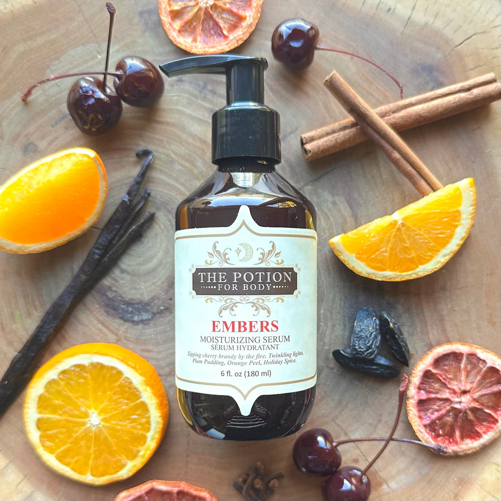 The Potion Cosmetics Embers Body Potion bottle with warm festive background