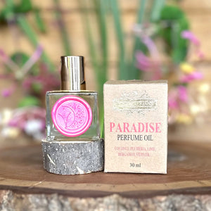 Paradise perfume oil bottle and packaging by The Potion Cosmetics on a wooden surface with a blurred natural background