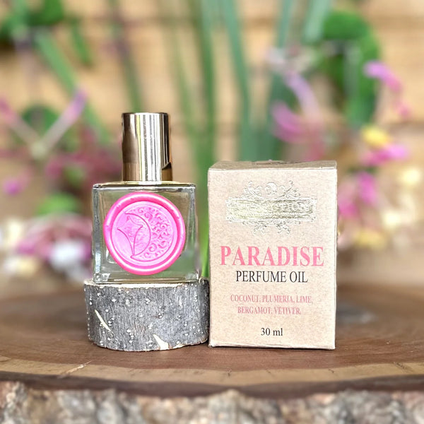 Paradise perfume oil bottle and packaging by The Potion Cosmetics on a wooden surface with a blurred natural background