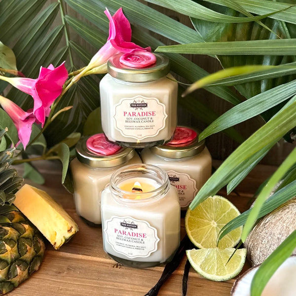 Candles labeled 'Paradise' with tropical elements like a pineapple, lime, and flowers on a wooden surface.