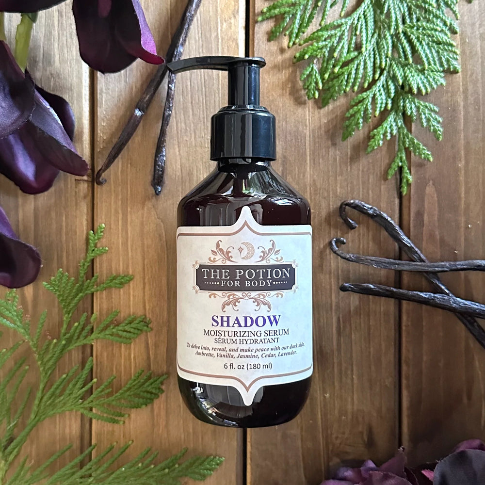 THE POTION COSMETICS Shadow Body Potion bottle surrounded by cedar, jasmine, and vanilla, evoking a deep, sultry floral musk fragrance.