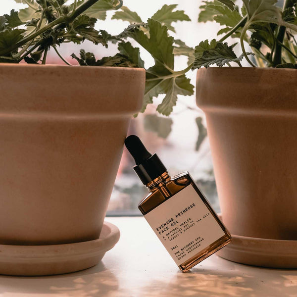 Bottle of face oil with a dropper next to potted plants on a windowsill