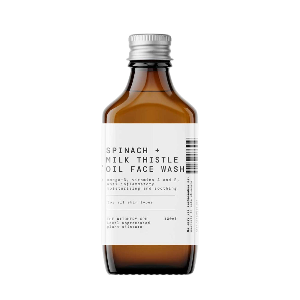 An amber glass bottle of Spinach + Milk Thistle Oil Face Wash by The Witchery CPH, featuring a white label and a silver metal cap, set against a plain white background.