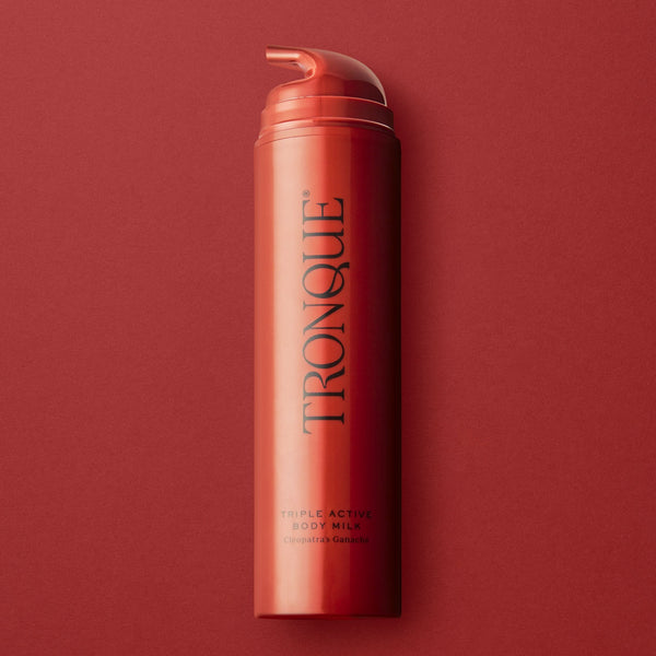 Red bottle of Tronque body milk on a red background. TRONQUE Triple Active Body Milk