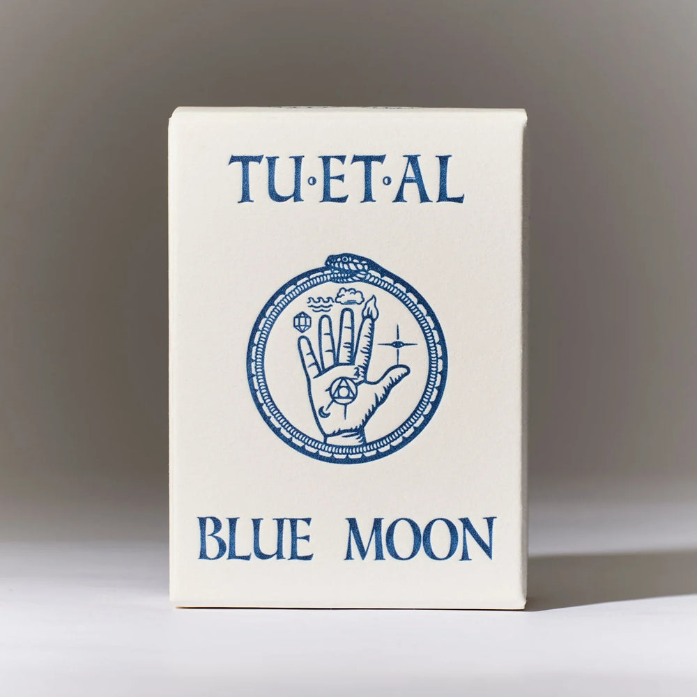 A dark charcoal gray bar of TU·ET·AL Blue Moon soap resting on top of its white cardboard packaging box, which features the scent name 'BLUE MOON' in blue lettering.