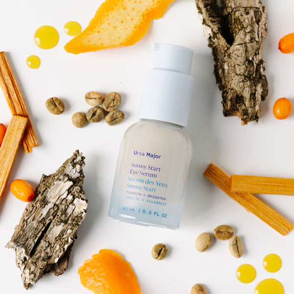 Ursa Major Sunny Start Eye Serum bottle surrounded by natural elements on a white background