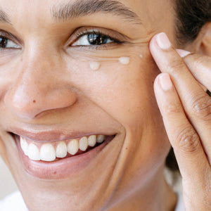 Close-up of a woman applying eye serum to their face with a blurred background