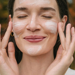 Woman applying URSA MAJOR Vital Spring Hydration Mask to her face with a blurred natural background