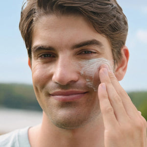 Man applying URSA MAJOR Vital Spring Hydration Mask to his face outdoors with a blurred natural background