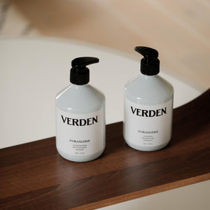 Two white VERDEN D'ORANGERIE Shampoo and Conditioner placed on a dark wooden surface in a softly lit indoor setting.