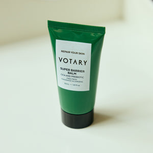Green tube of Votary Super Barrier Balm on a light beige background