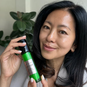 Woman holding a green skincare product with a plant in the background.  VOTARY Ultimate Rich Cream